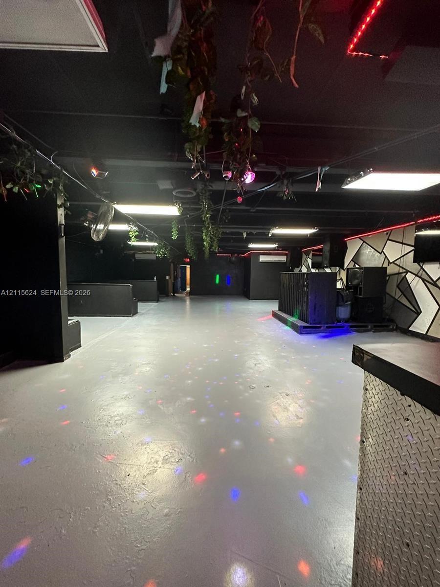 Open-concept interior featuring smooth concrete flooring, geometric wall paneling, built-in diamond-plate bar facade, and exposed ceiling with integra