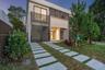 Modern two-story residence featuring a smooth stucco exterior, horizontal metal privacy screening, integrated balcony, and a permeable paver driveway 