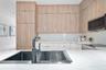 Kitchen featuring floor-to-ceiling wood-finish cabinetry, white stone-finish countertops, matte black single-handle faucet, integrated stainless steel