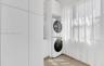 Laundry space featuring floor-to-ceiling white cabinetry, integrated stacking appliance housing, and tile flooring