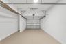 Enclosed garage featuring finished concrete flooring, painted walls, an automated sectional door, and overhead lighting