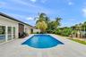In-ground swimming pool with stone-tile decking, waterfront bulkhead, and mature tropical landscaping