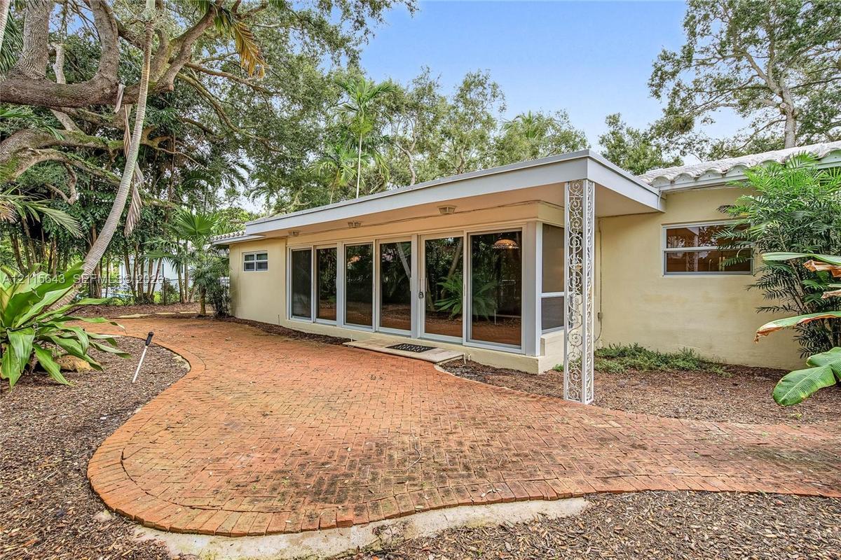 Stucco exterior featuring a covered patio, brick-paver hardscaping, decorative wrought iron support column, and floor-to-ceiling glass panel sliding d