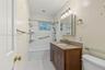 Bathroom featuring a vanity with wood-finish cabinetry, stone-composite countertop, integrated medicine cabinet, tile-surround bathtub, and geometric 