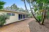 Stucco exterior featuring a curved brick walkway, series of glass sliding doors, and a tile roof set among mature tropical landscaping