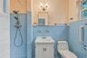 Bathroom featuring blue tile wainscoting, pedestal-style vanity with louvered cabinet doors, dual-head shower fixture, wall-mounted light fixture, and