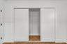 Dual sliding Shaker-style doors with a matte white finish and herringbone wood-finish flooring