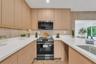 Kitchen featuring light wood-finish cabinetry, quartz countertops, vertical textured backsplash, stainless steel microwave, and chevron-patterned floo