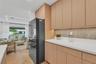 Flat-panel light wood cabinetry featuring under-cabinet lighting, solid surface countertops, textured backsplash, and herringbone-pattern wood-finish 