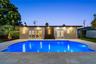 Swimming pool with stone-tile decking, dual sets of French doors, recessed ceiling lighting, and vertical exterior wall-mounted fixtures