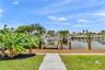 Waterfront property featuring a composite deck, private boat lift, and anchored wooden pilings, complemented by a paver stone walkway and tropical lan