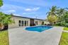Rear exterior featuring an in-ground swimming pool, expansive stone paver patio, multi-panel glass door systems, and mature landscaping