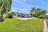 Backyard featuring a concrete pool deck, in-ground swimming pool, manicured lawn, tropical landscaping, and a waterfront bulkhead