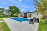 In-ground swimming pool with light-toned stone paver decking, exterior wall lighting, and double-glass door entry