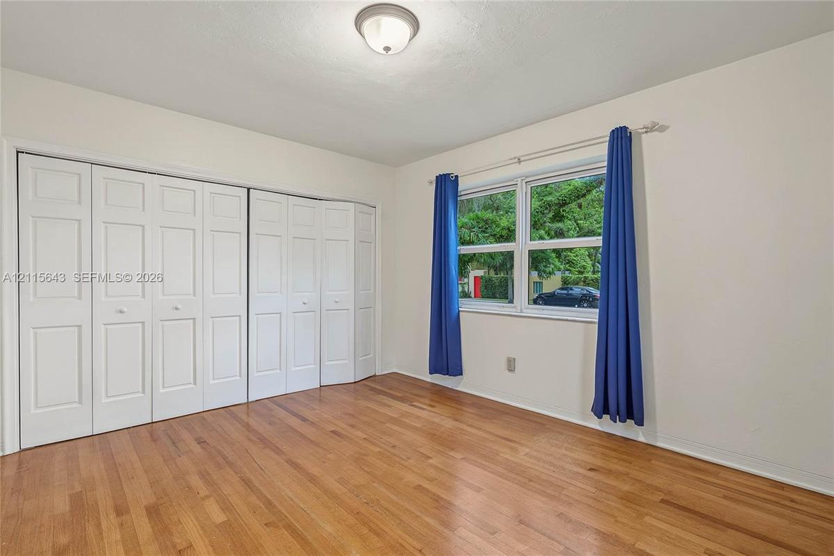 Room featuring wood-finish flooring, white panel-style bi-fold closet doors, a multi-pane window, and a central ceiling-mounted light fixture