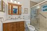 Bathroom featuring wood cabinetry, integrated vanity top with a rectangular sink, three-light fixture, and a tiled shower enclosure with sliding glass