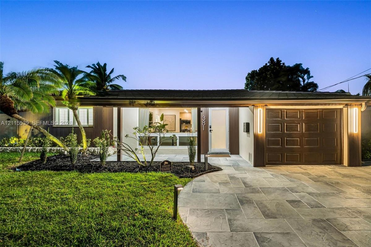 Single-story exterior featuring a natural stone-patterned paved driveway, integrated vertical exterior wall lighting, and landscaped front lawn with m