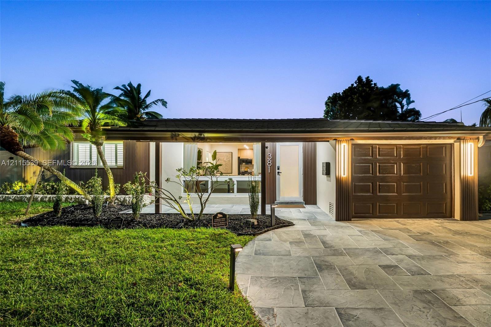 Single-story exterior featuring a natural stone-patterned paved driveway, integrated vertical exterior wall lighting, and landscaped front lawn with m