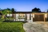 Single-story exterior featuring a natural stone-patterned paved driveway, integrated vertical exterior wall lighting, and landscaped front lawn with m