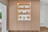 Floor-to-ceiling cabinetry with light wood-finish veneer, integrated recessed display shelving, built-in task lighting, white solid-surface countertop