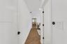 Hallway featuring wood-finish flooring in a herringbone pattern, matte black door hardware, and crisp white walls
