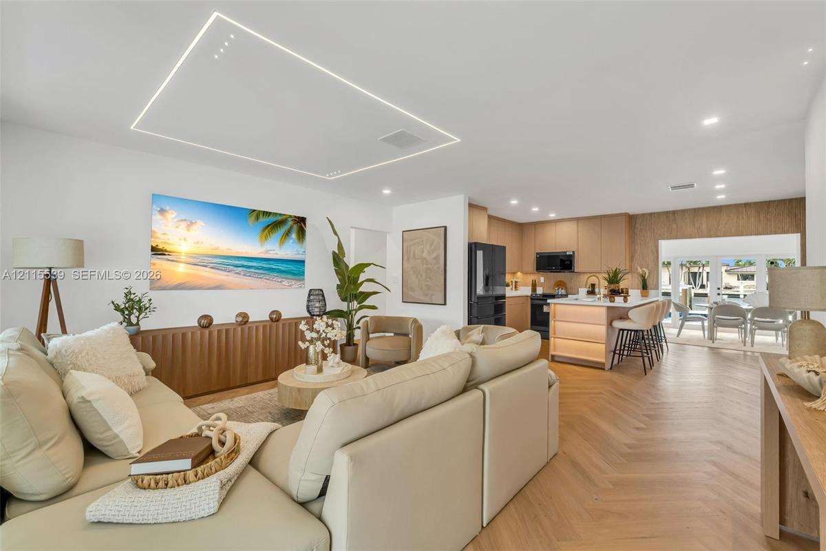 Open-concept living space featuring wood-finish flooring in a herringbone pattern, a recessed rectangular tray ceiling with perimeter lighting, recess