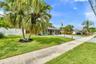 Single-story residence featuring a paver driveway, an attached garage, white privacy fencing, and established palm trees