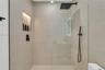 Walk-in shower featuring large-format neutral tile, frameless glass enclosure, matte black rainfall showerhead, integrated handheld sprayer, and reces