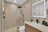 Bathroom featuring a wood-finish vanity with a light-toned stone countertop, a glass-enclosed walk-in shower with matte black fixtures, a built-in sho