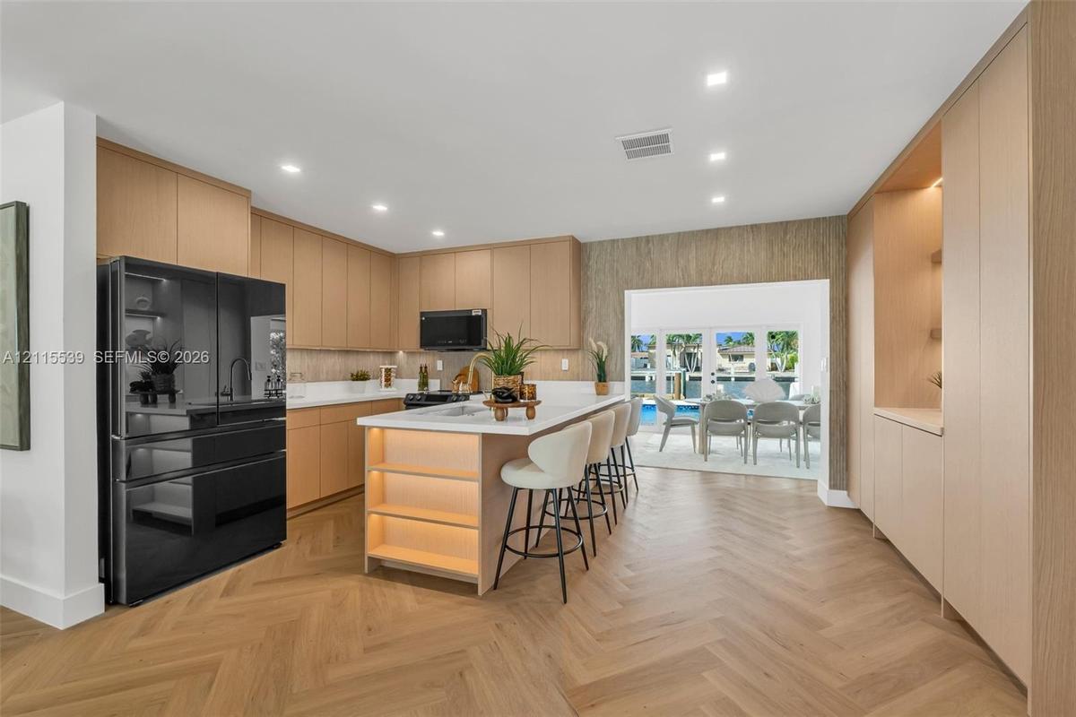 Kitchen featuring custom light wood cabinetry, white stone countertops, herringbone patterned wood-finish flooring, recessed lighting, and a center is