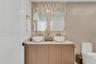 Double vanity featuring wood-finish cabinetry, white vessel sinks, gold-tone wall-mounted faucets, arched mirrors, and a patterned tile backsplash