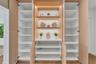 Custom built-in cabinetry featuring light wood-finish veneer, integrated LED shelf lighting, fixed white shelving, and a central solid-surface counter