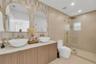 Dual vanity featuring vessel sinks, quartz countertops, wood-finish cabinetry, arched mirrors with gold-toned frames, and a walk-in shower with a glas