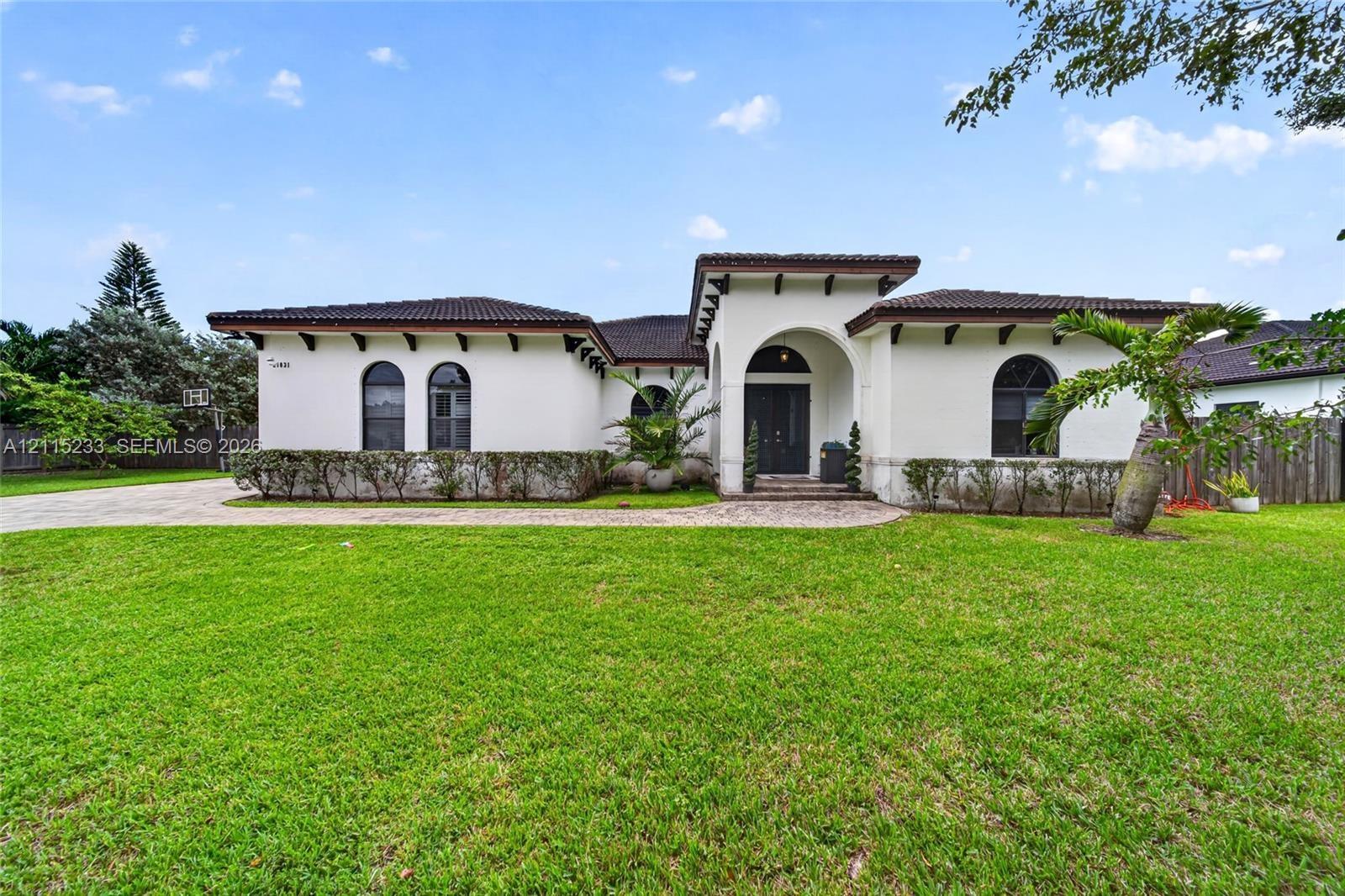 Stucco exterior featuring arched windows, tile roofing, decorative exposed rafters, and a paved walkway