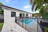 Exterior featuring a swimming pool, stone-paver patio, covered porch, and mature palm trees