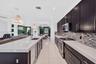 Kitchen featuring dark cabinetry, expansive quartz countertops, a stone mosaic tile backsplash, stainless steel appliances, and tile flooring