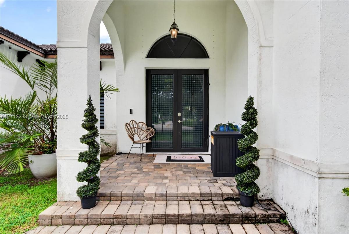 Covered entryway featuring a stone-paver porch, arched stucco facade, semi-circular transom window, and double doors with grid-pattern glass inserts