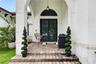 Covered entryway featuring a stone-paver porch, arched stucco facade, semi-circular transom window, and double doors with grid-pattern glass inserts