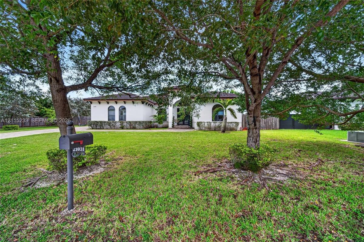 Stucco exterior featuring arched windows, tile roofing, and an expansive front lawn with mature canopy trees