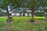 Stucco exterior featuring arched windows, tile roofing, and an expansive front lawn with mature canopy trees