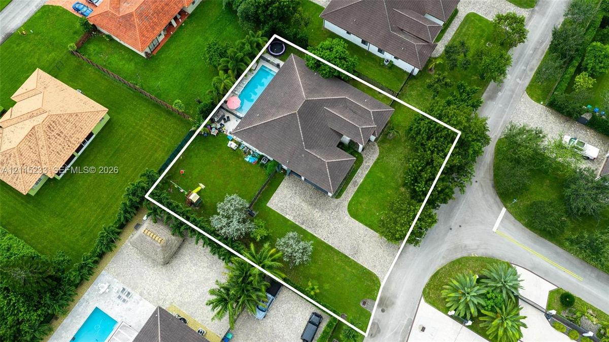 Aerial perspective featuring a hip-roof structure, a rectangular swimming pool, and a paver driveway on a landscaped lot