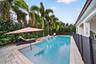 In-ground swimming pool featuring a tanning ledge, integrated water feature, paver patio, and surrounding palm trees