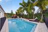 In-ground swimming pool featuring a tiered water feature, light-toned stone pool decking, and mature palm trees