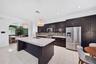 Kitchen featuring dark cabinetry, expansive center island with stone-finish countertop, stainless steel appliances, decorative tile backsplash, and ov