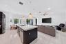 Open-concept area featuring polished tile flooring, a center island with a stone-composite countertop, stainless steel kitchen appliances, neutral-ton