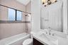 Bathroom featuring a dark-finish vanity with a white countertop, large rectangular mirror, soaking tub with horizontal tile surround, and a glass-tile
