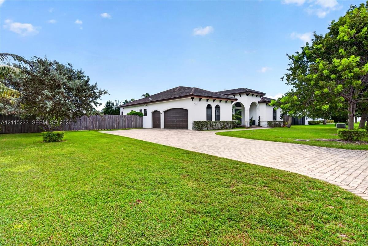 Stucco exterior featuring an arched entryway, decorative corbels, a multi-car garage with arched doors, and a paver driveway