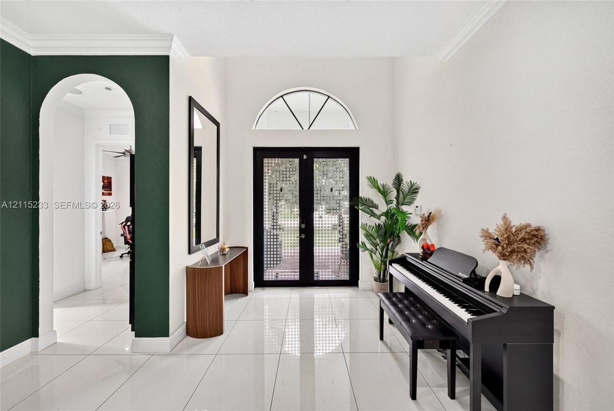 Foyer featuring large-format tile flooring, double glass-paned entry doors, a semi-circular transom window, and a decorative arched passage