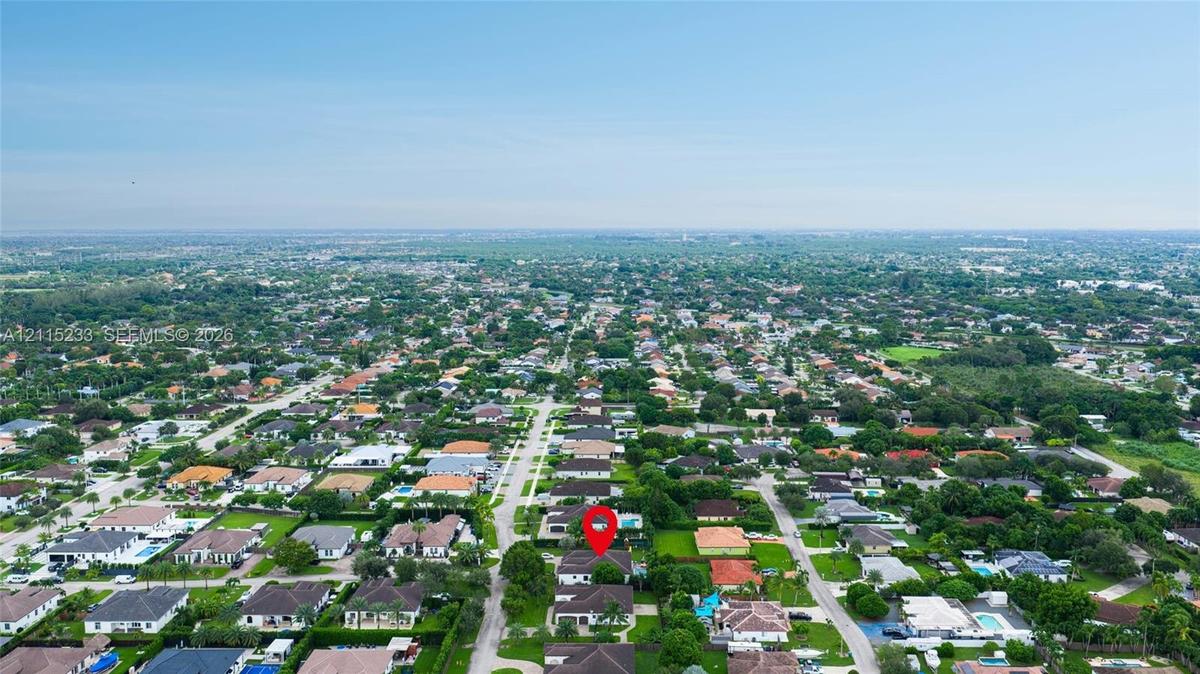 Aerial perspective of a single-story residence situated within a suburban neighborhood featuring mature canopy trees, paved roadways, and residential 