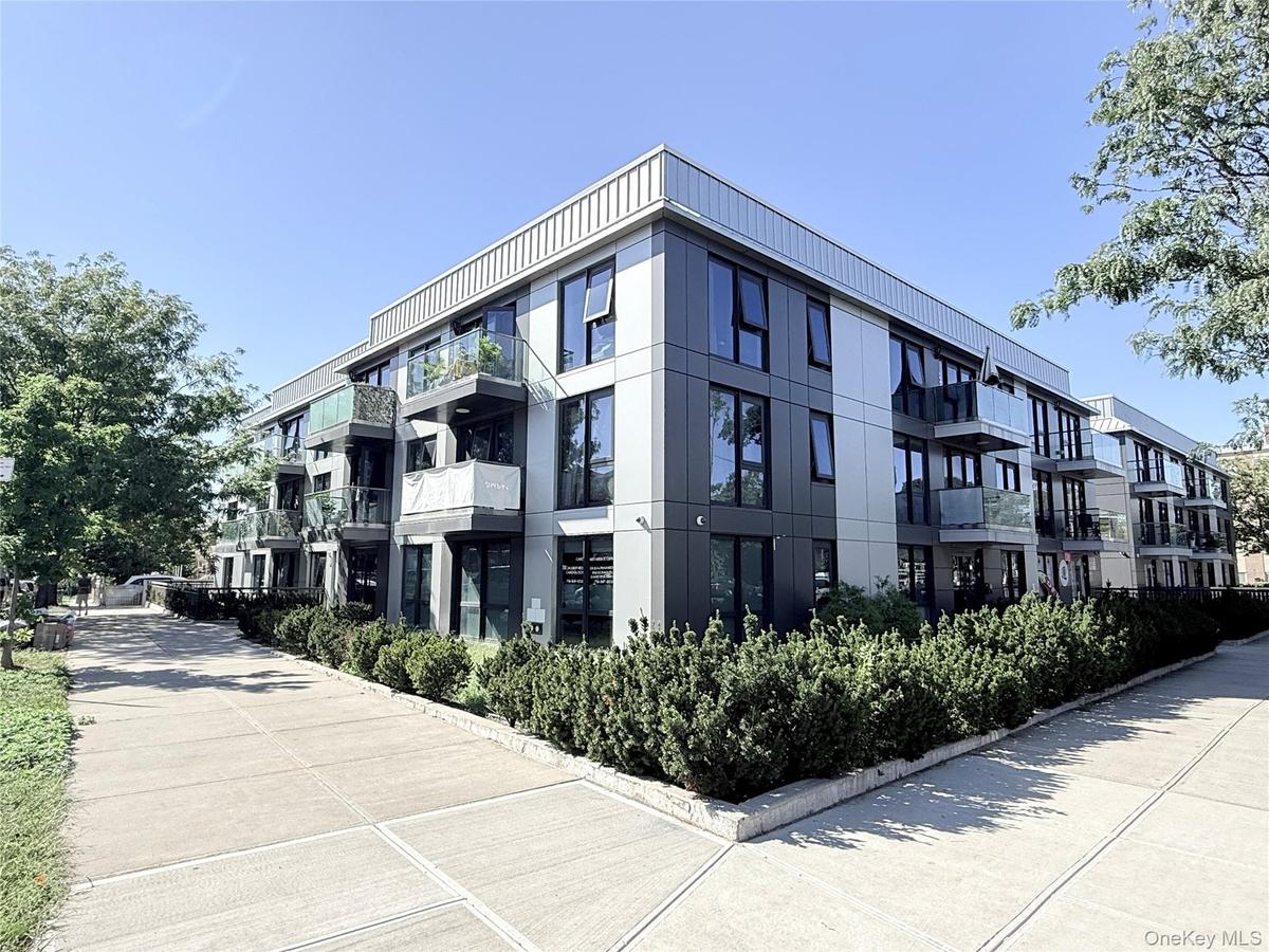 Contemporary multi-story building featuring a facade with dark and light panels, multiple glass-railed balconies, and extensive ground-level shrubbery